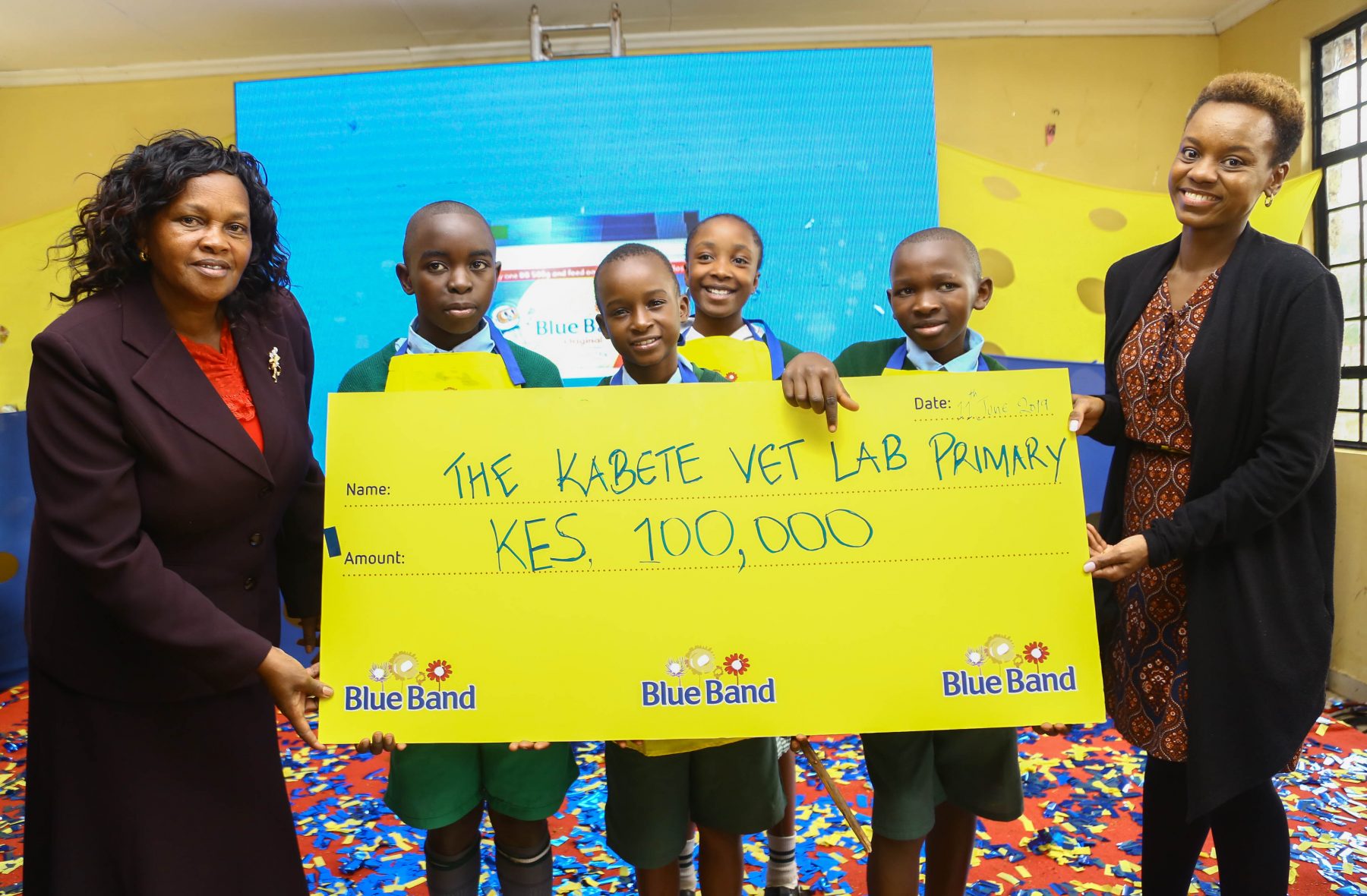 From left: Hellen Mugo, Head Teacher Kabete Vet lab primary School together with the students of Vet lab Primary School receive a dummy cheque worth Ksh. 100,000 from Jacky Mungai, Upfield Head of Marketing East and Southern Region during the launch of Blue Band Good Breakfast and Social Mission Campaign at Kabete Vet Lab Primary School.
