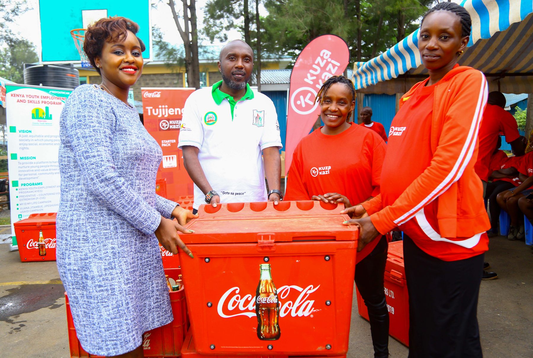 Coca-Cola Sustainability Coordinator Public Affairs and Communications, Victoria Macharia (Left), in company of One-Stop Youth Program Coordinator, Wainaina Muiruri (second left), present a Coca-Cola sales starter pack inclusive of a cooler box and crates of Coca-Cola beverages to Kuza Kazi beneficiaries, Wincete Karemi (Right) and Doreen Omwenga.